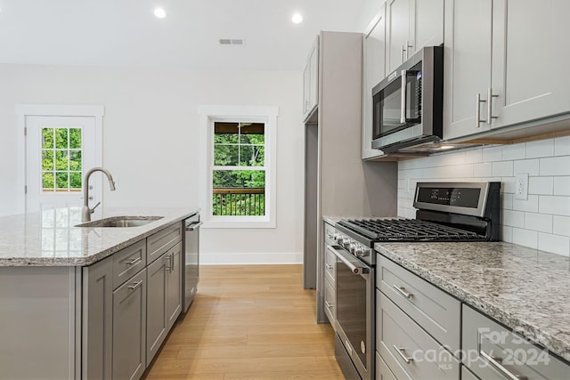 kitchen featuring appliances with stainless steel finishes, sink, light stone counters, light wood-type flooring, and a kitchen island with sink