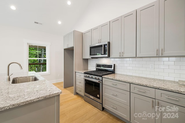 kitchen featuring lofted ceiling, gray cabinetry, stainless steel appliances, light stone countertops, and sink