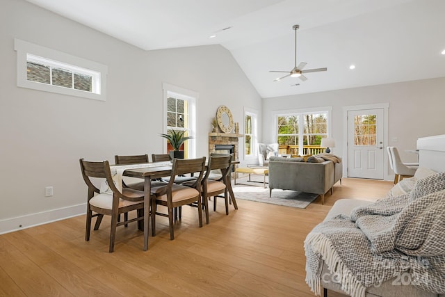 dining space featuring light wood-type flooring, ceiling fan, vaulted ceiling, and a stone fireplace