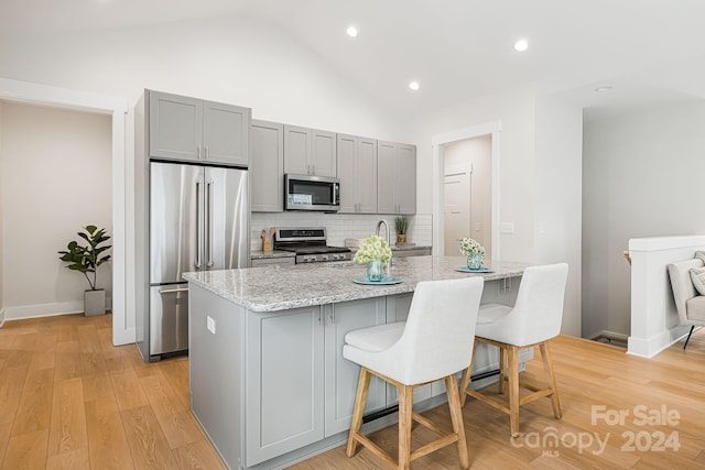 kitchen featuring a kitchen breakfast bar, gray cabinetry, stainless steel appliances, and light stone counters