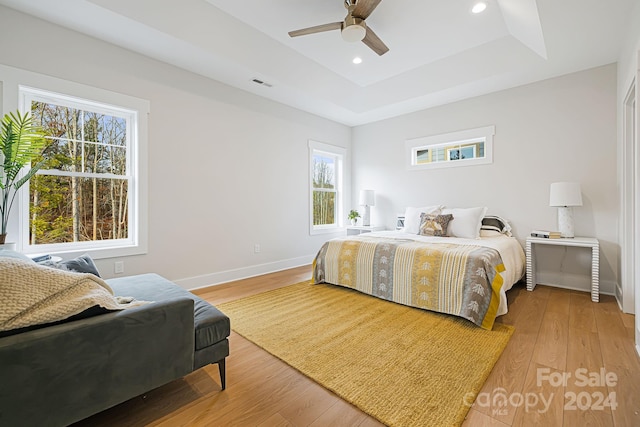 bedroom with light wood-type flooring, ceiling fan, and a raised ceiling