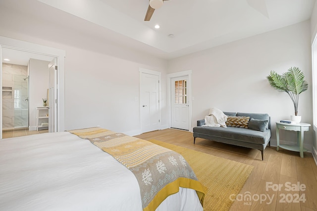 bedroom with connected bathroom, ceiling fan, light hardwood / wood-style flooring, and a tray ceiling