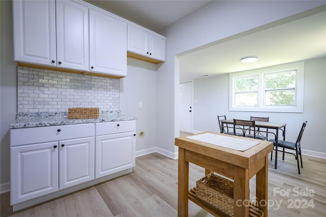 kitchen with white cabinetry, decorative backsplash, light stone countertops, and light wood-type flooring