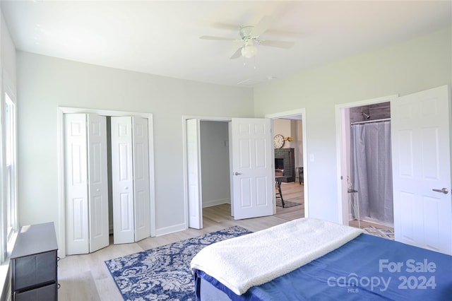 bedroom featuring multiple closets, a brick fireplace, ceiling fan, and light hardwood / wood-style flooring