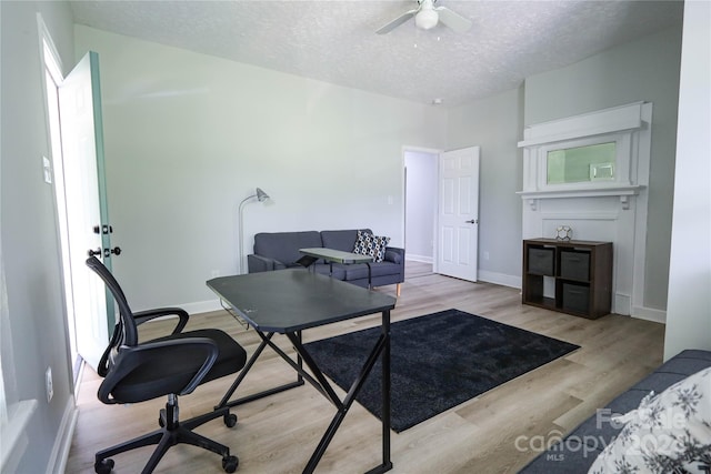 home office featuring ceiling fan, light hardwood / wood-style flooring, and a textured ceiling