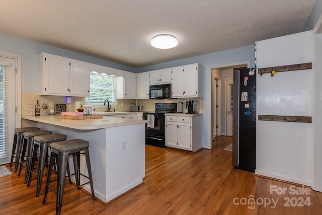 kitchen with a breakfast bar, black appliances, white cabinetry, sink, and kitchen peninsula