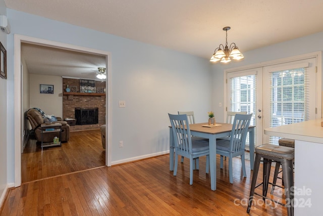 dining area with hardwood / wood-style flooring, a chandelier, a brick fireplace, and french doors