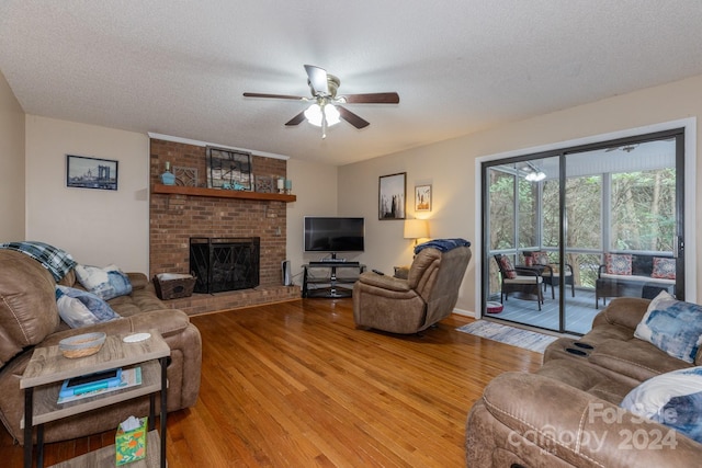 living room featuring ceiling fan, a fireplace, a textured ceiling, and light wood-type flooring