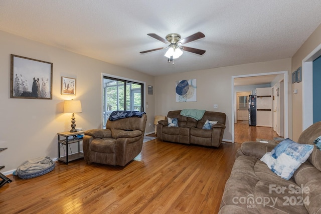 living room with ceiling fan, light wood-type flooring, and a textured ceiling