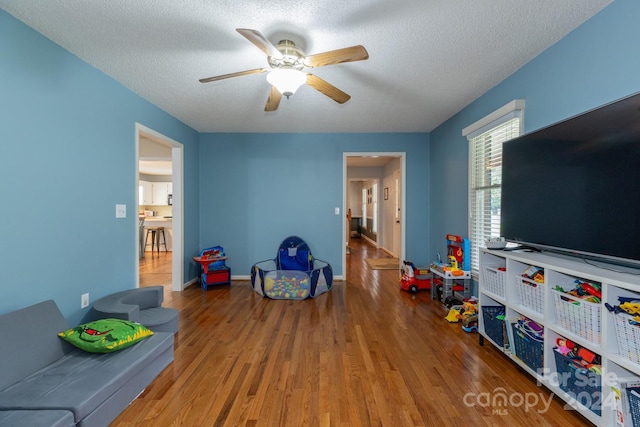 rec room with ceiling fan, wood-type flooring, and a textured ceiling