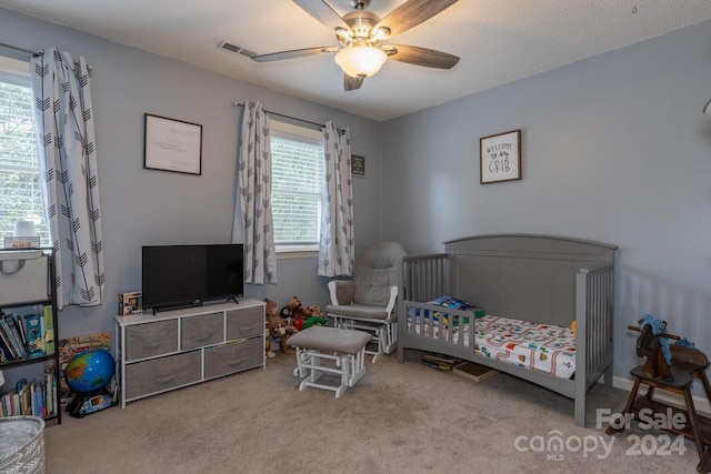 bedroom featuring light carpet, a textured ceiling, a crib, and ceiling fan