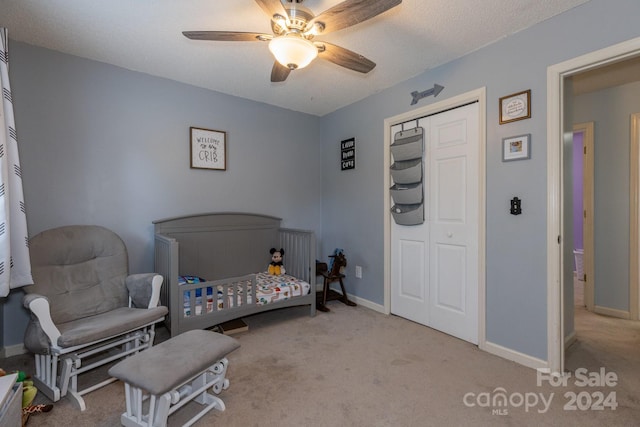 bedroom featuring light colored carpet, a textured ceiling, a closet, ceiling fan, and a crib