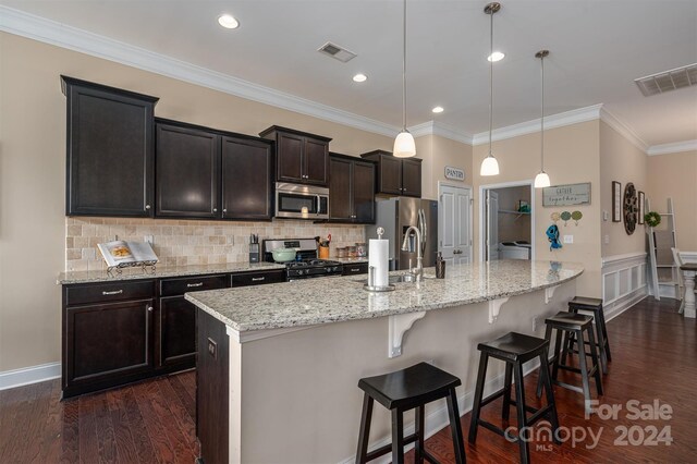 kitchen featuring appliances with stainless steel finishes, pendant lighting, crown molding, an island with sink, and dark hardwood / wood-style flooring