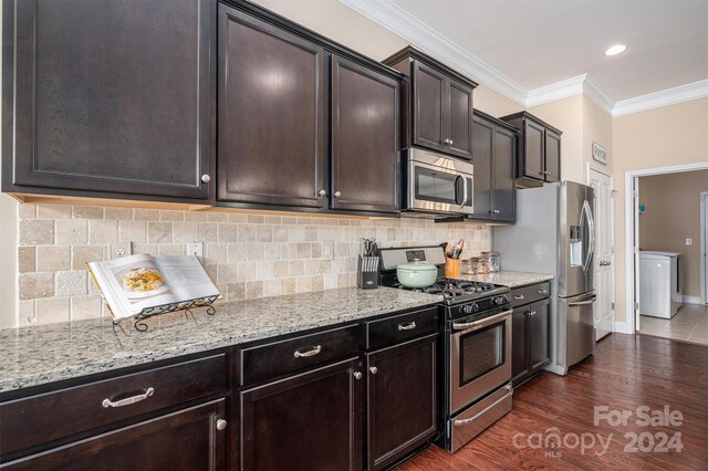 kitchen with appliances with stainless steel finishes, backsplash, washer / dryer, light stone countertops, and dark wood-type flooring