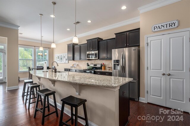 kitchen featuring a kitchen island with sink, dark hardwood / wood-style floors, appliances with stainless steel finishes, decorative light fixtures, and ornamental molding