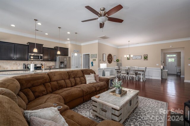 living room featuring ornamental molding, ceiling fan with notable chandelier, and dark wood-type flooring