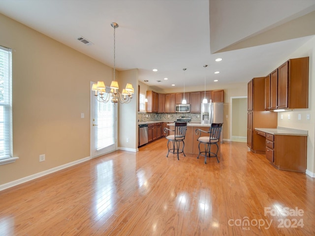 kitchen featuring light wood-type flooring, stainless steel appliances, decorative light fixtures, and a notable chandelier