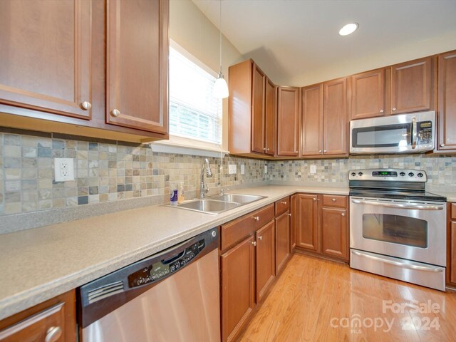 kitchen featuring tasteful backsplash, light hardwood / wood-style floors, appliances with stainless steel finishes, decorative light fixtures, and sink