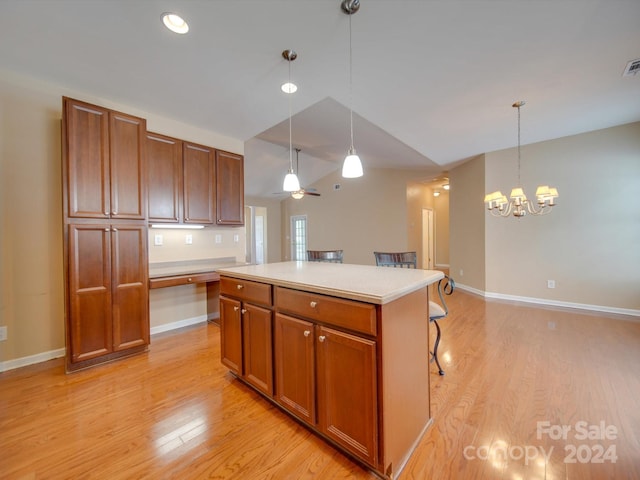 kitchen with ceiling fan with notable chandelier, pendant lighting, a kitchen island, a breakfast bar, and light hardwood / wood-style flooring