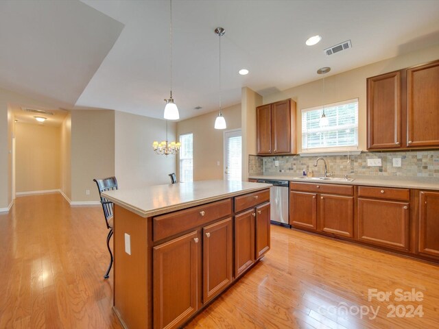 kitchen with stainless steel dishwasher, hanging light fixtures, decorative backsplash, a kitchen island, and light hardwood / wood-style flooring