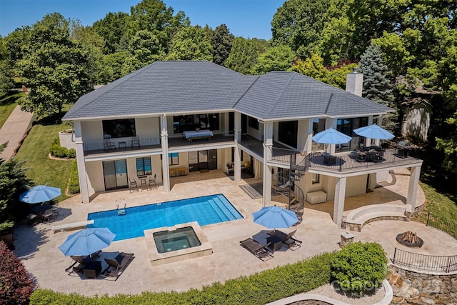 rear view of property with a swimming pool with hot tub, an outdoor fire pit, a balcony, and a patio