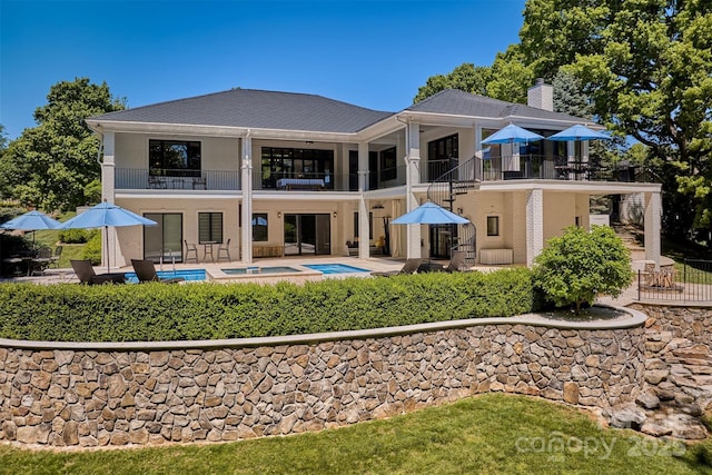 back of house featuring a swimming pool with hot tub, a balcony, and a patio