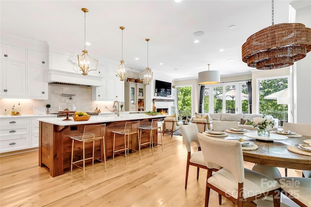 kitchen with light hardwood / wood-style floors, decorative backsplash, a spacious island, hanging light fixtures, and white cabinets