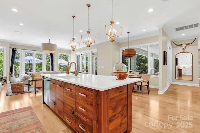 kitchen with a wealth of natural light, an island with sink, sink, hanging light fixtures, and light hardwood / wood-style flooring