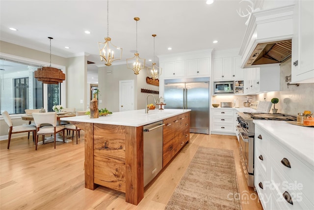 kitchen with pendant lighting, sink, built in appliances, white cabinetry, and an island with sink