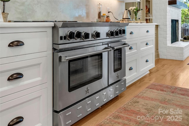 kitchen with a brick fireplace, light hardwood / wood-style floors, white cabinets, and range with two ovens