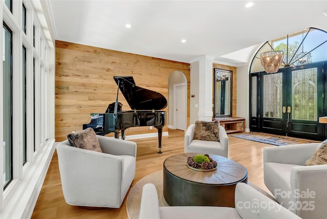 living room with light wood-type flooring, a chandelier, french doors, and wooden walls