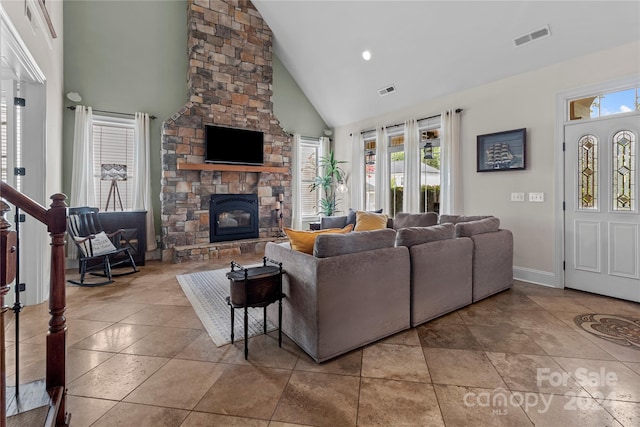 living room with plenty of natural light, a stone fireplace, high vaulted ceiling, and light tile patterned floors