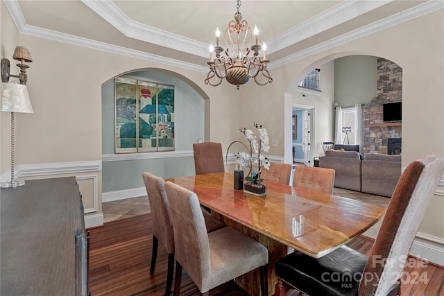 dining space with crown molding, a stone fireplace, dark wood-type flooring, and a chandelier