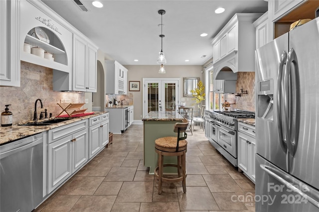 kitchen with appliances with stainless steel finishes, pendant lighting, white cabinetry, a center island, and light stone counters