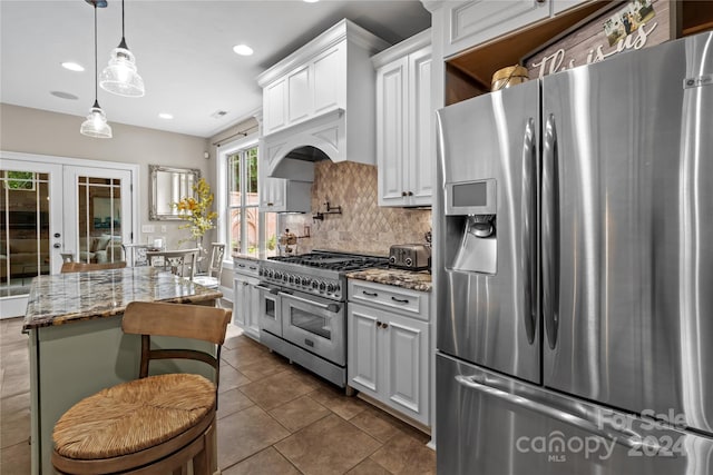 kitchen with appliances with stainless steel finishes, light stone counters, white cabinets, a kitchen island, and french doors