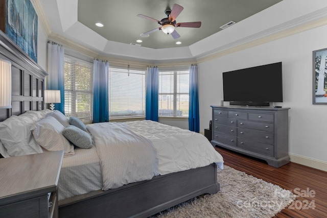 bedroom featuring dark hardwood / wood-style floors, ceiling fan, ornamental molding, and a tray ceiling