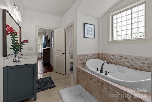 bathroom with tiled tub, vanity, and toilet