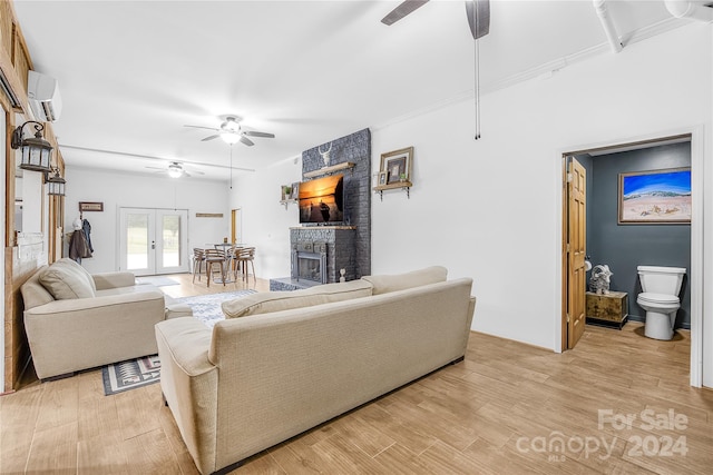 living room featuring a fireplace, a wall mounted AC, ceiling fan, light wood-type flooring, and french doors