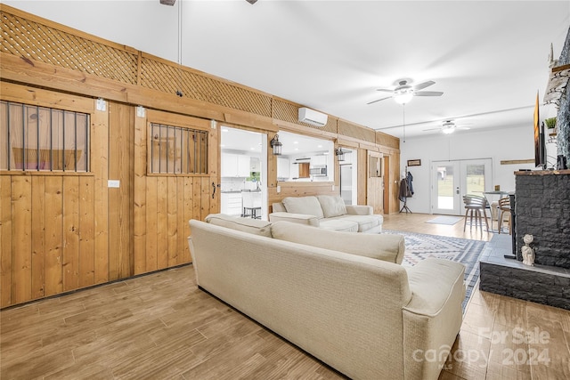 living room with light hardwood / wood-style flooring, ceiling fan, a wall unit AC, french doors, and wood walls