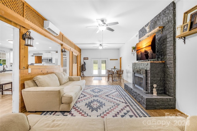 living room with a fireplace, sink, hardwood / wood-style flooring, a wall unit AC, and french doors