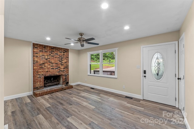 entrance foyer with ceiling fan, a brick fireplace, and light hardwood / wood-style floors