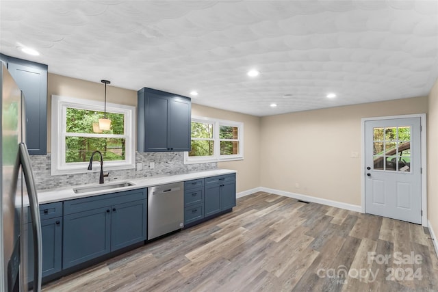 kitchen with stainless steel appliances, sink, pendant lighting, and light hardwood / wood-style floors