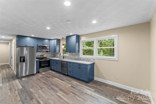 kitchen with hardwood / wood-style floors, tasteful backsplash, sink, stainless steel appliances, and blue cabinetry