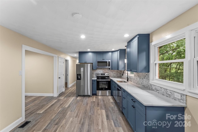 kitchen featuring sink, appliances with stainless steel finishes, light stone countertops, hardwood / wood-style floors, and decorative backsplash