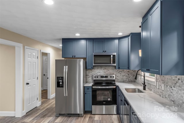 kitchen featuring appliances with stainless steel finishes, sink, light hardwood / wood-style floors, light stone countertops, and blue cabinetry