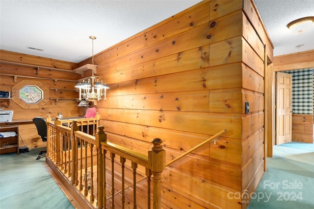 hall featuring wood walls, a notable chandelier, carpet, and a textured ceiling