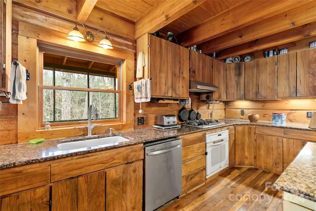 kitchen with sink, light hardwood / wood-style flooring, appliances with stainless steel finishes, beam ceiling, and wood walls