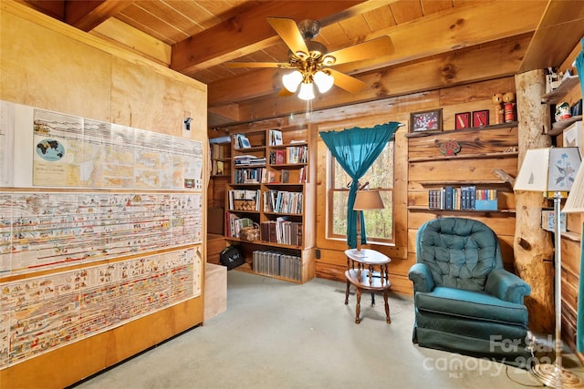 sitting room with ceiling fan, wood ceiling, beamed ceiling, and wood walls