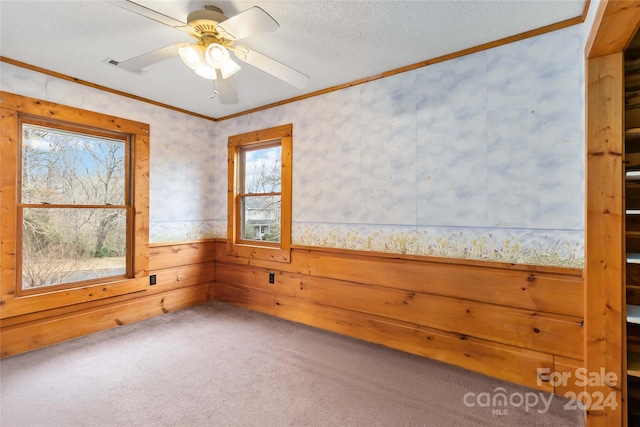 carpeted spare room with ceiling fan, ornamental molding, wooden walls, and a textured ceiling