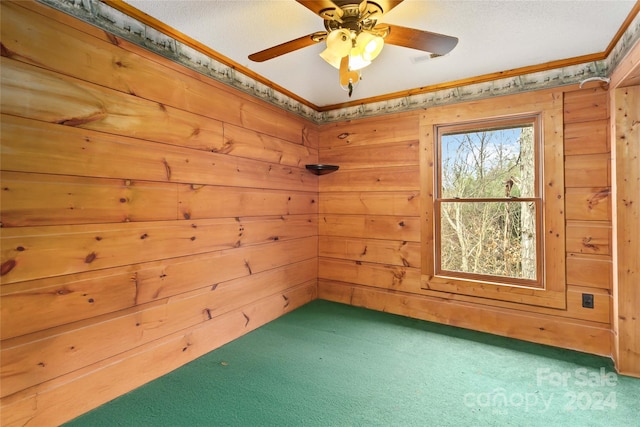 carpeted empty room with crown molding, ceiling fan, and wood walls